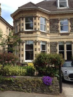 a car is parked in front of a large house with many windows and bushes around it