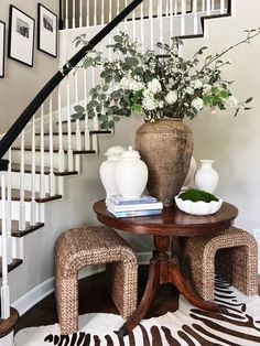 a vase with flowers sitting on top of a table next to two stools and a zebra print rug