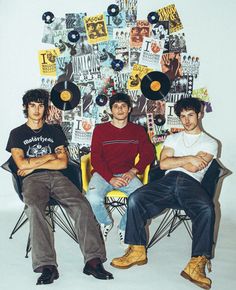 three young men sitting next to each other in front of a wall with records on it