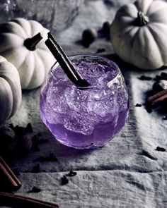 a purple drink in a glass with ice and cinnamon sticks on the table next to pumpkins