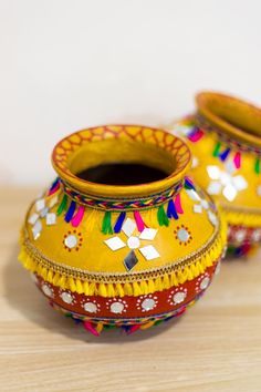 two yellow vases sitting on top of a wooden table next to each other with colorful designs