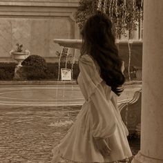 a woman standing in front of a fountain with her long hair blowing in the wind