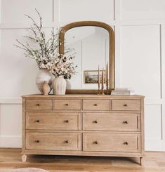 a dresser with a mirror and vase on top of it in front of a white wall