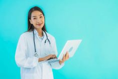 a female doctor is holding a laptop and smiling at the camera while standing in front of a blue background