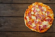 a pizza sitting on top of a wooden table covered in cheese and ham toppings