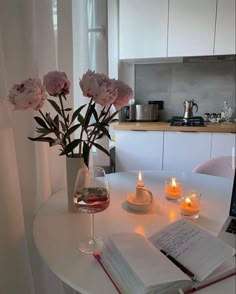 a vase with flowers and candles on a table in front of a laptop, next to an open book