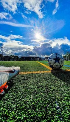 two soccer balls sitting on top of a green field with yellow lines and blue sky in the background