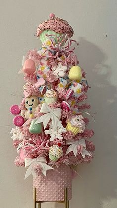 a pink christmas tree decorated with teddy bears and other toys on a gold stand against a white wall