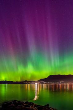 the aurora bore is shining brightly in the night sky over water and mountains, with bright lights