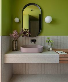 a bathroom with green walls and a pink sink in front of a round mirror on the wall