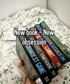 a person holding a stack of books in front of a bed with the words new book = new obesession