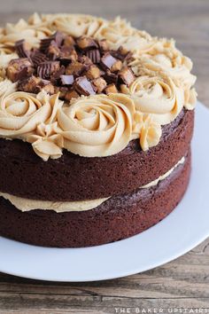 a chocolate cake topped with frosting and nuts on a white plate next to a wooden table