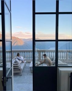 two people sitting in chairs on a balcony with mountains in the background