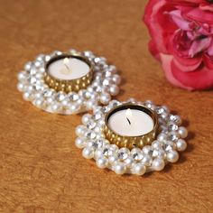 two pearls and a candle are sitting on a table next to a pink flower with a rose in the background