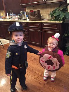 two young children dressed in costumes standing next to each other on a kitchen floor with wooden cabinets