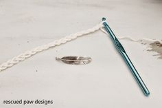 a crochet hook with a feather on it next to a blue knitting needle