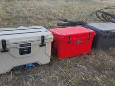 three coolers sitting on the ground in an open field, one red and one black