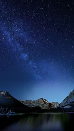 the night sky is filled with stars above mountains and water, as seen from a lake