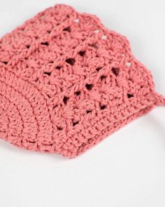 a pink crochet dishcloth on a white surface with a hook in the middle