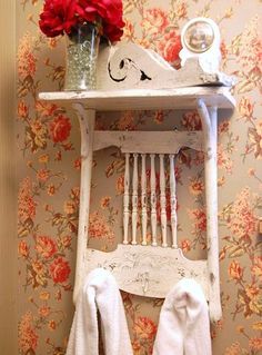 a white shelf with flowers and towels on it next to a wallpapered wall