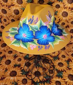 Hand painted mustard yellow sun hat with a touch of bright blue floral design Yellow Bohemian Straw Hat With Short Brim, Yellow Bohemian Straw Hat With Curved Brim, Bohemian Yellow Straw Hat With Short Brim, Yellow Bohemian Fedora Straw Hat, Tropical Multicolor Spring Hats, Yellow Bohemian Wide Brim Straw Hat, Handmade Yellow Wide Brim Straw Hat, Tropical Hats With Curved Brim For Spring, Yellow Panama Hat With Curved Brim For Spring