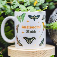 a white coffee mug with butterflies on it and the words, antsocial moth