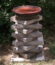 a large stack of rocks with a bowl on top sitting in the grass next to some bushes