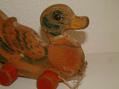 an old wooden ducky toy with red wheels on a white surface, next to a wall