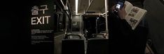 a person reading a book while on a subway train with an exit sign in the background