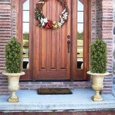 two potted plants are sitting on the front porch next to a wooden door with wreaths