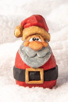 a santa clause figurine sitting in the snow with his hat on and eyes wide open