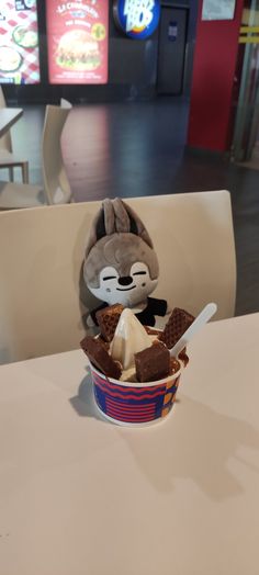 a stuffed animal sitting in a cup filled with ice cream and waffles on top of a table