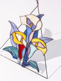 a stained glass flower is hanging from a chain on a white surface with shadows in the background