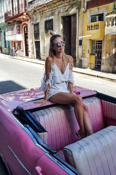 a woman sitting on top of a pink convertible car