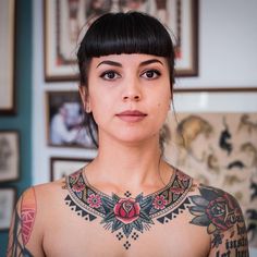 a woman with lots of tattoos on her chest looking at the camera while standing in front of pictures