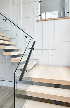 a staircase with glass railing and wood treads in a white room next to a wooden floor