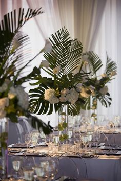 there is a vase with flowers and greenery on the table set for an event