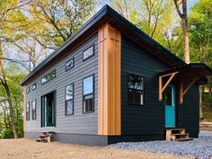 the tiny house is built on gravel and has blue door, windows, and steps