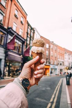 a person holding up an ice cream cone in the middle of a street with buildings on both sides