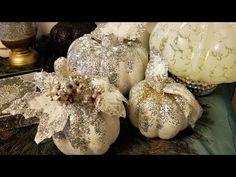 some white pumpkins are sitting on a table with silver and gold decorations around them