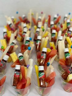 many small cups filled with different types of fruit and condiments on toothpicks