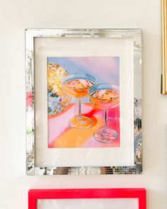 two framed pictures hang on the wall next to each other, one with an orange and pink drink in it