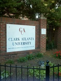 the sign for clark atlanta university in front of a fenced area with flowers and trees