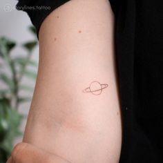 a small saturn tattoo on the back of a woman's right arm, which has a tiny ring around it