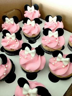 cupcakes with pink frosting and white bows are in a minnie mouse box