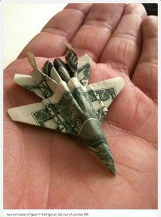 a dollar bill origami fighter jet in someone's hand