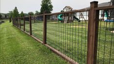 a fence that is in the grass next to a yard with a slide and play ground