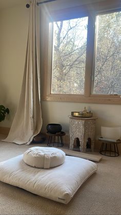 a white bed sitting under a window next to a wooden table with a potted plant on it