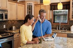 a man and woman are talking on the phone while standing in front of an oven