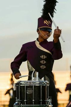 a man in a purple uniform is holding a drum and wearing a feathered hat